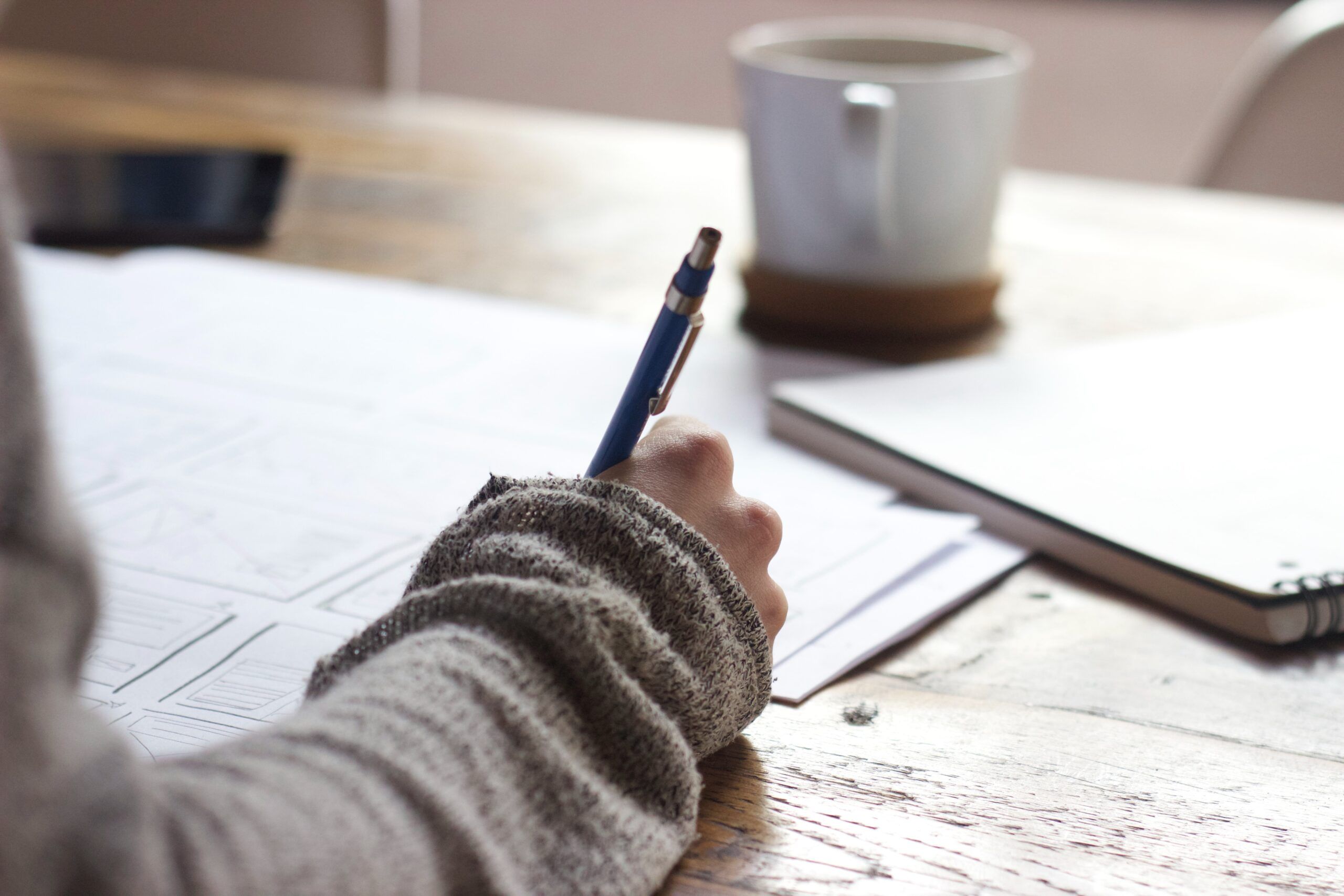 Image of a hand holding a pen and writing on a piece of paper on a table