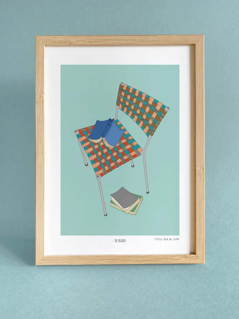 A print in a wood frame. The print features a colorful old lawn chair and open books. 