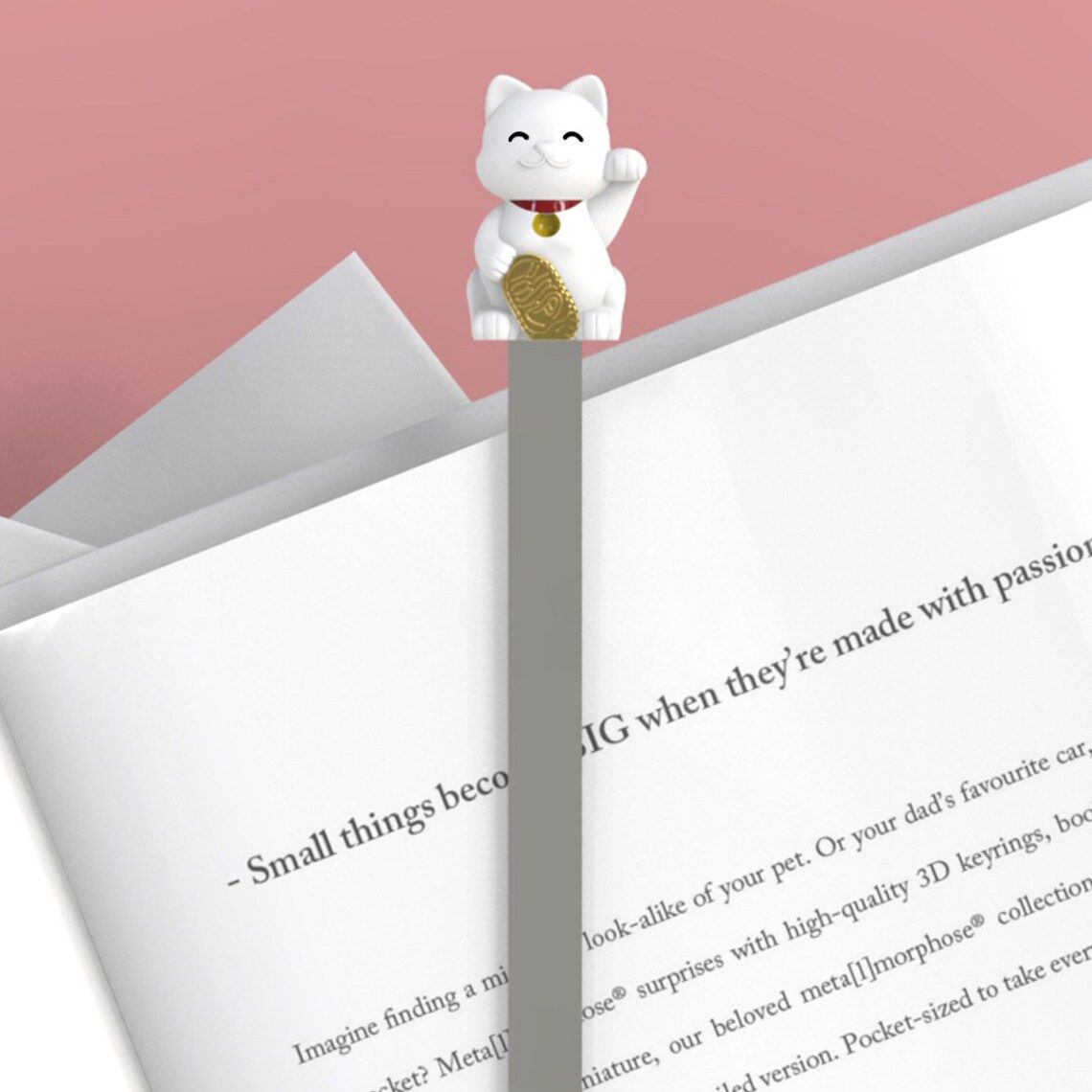 Image of a white lucky cat bookmark on an open book. 