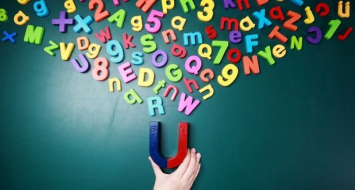 color letter shaped magnets being pulled by a half blue, half red u-shaped magnet being held by a light-skinned hand on a green board