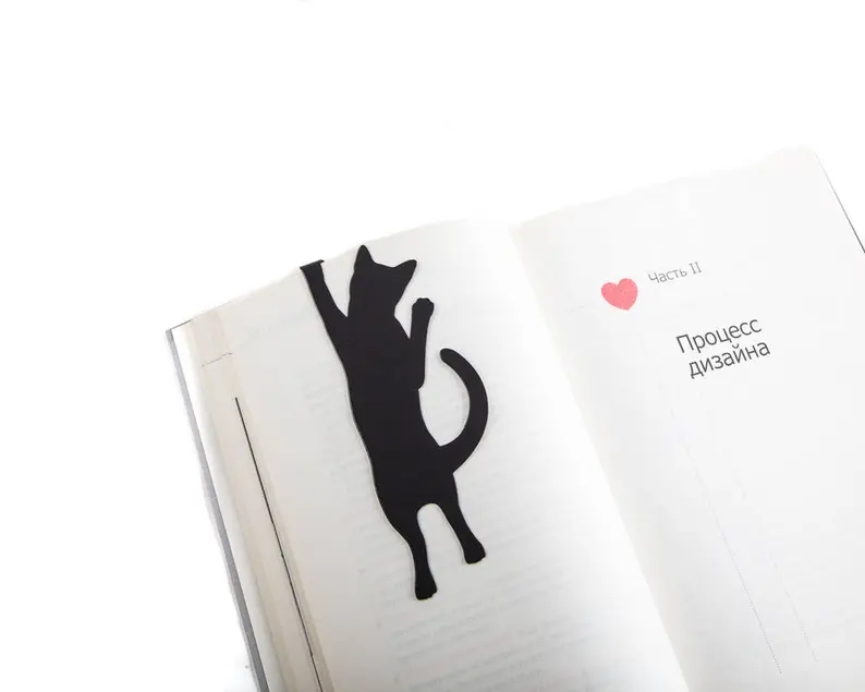 Image of a black metal bookmark. It's in the shape of a cat holding on to the top of a book page. 