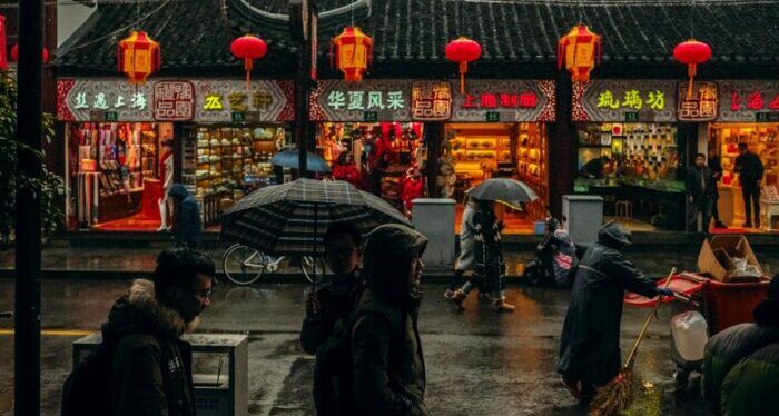 a photo of a Chinese street at night in the rain, with shops lit up and red lanterns hanging on a line