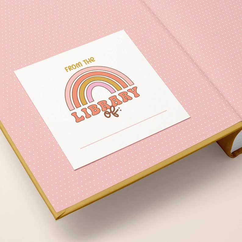 Image of a book plate inside a book with pink end papers. The bookplate features a pink and yellow pastel rainbow and says "from the library of."