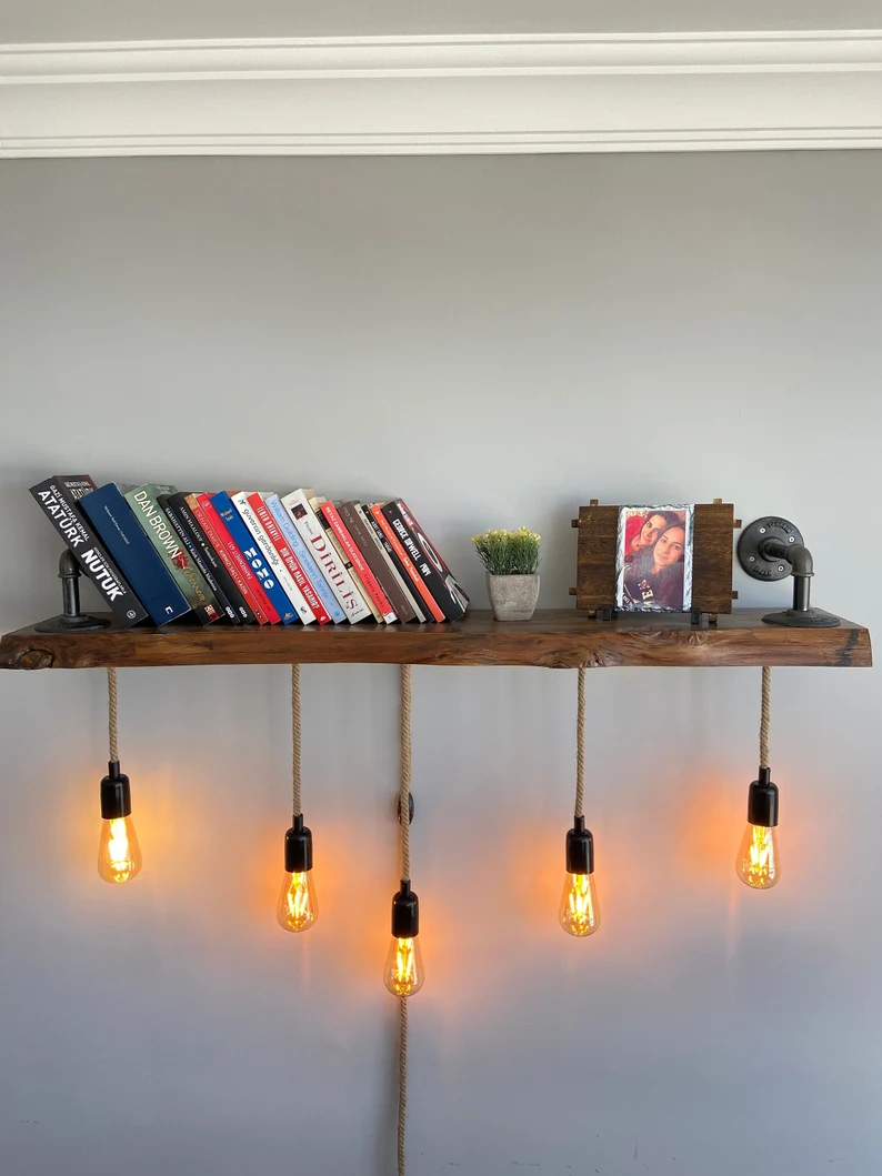 Image of a bookshelf made of heavy wood with a live edge. It has five Edison lights beneath it. 
