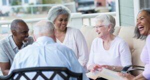 a diverse group of senior citizens seated in a circle. They are laughing and each holding a book in their lap.