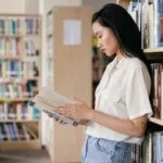 a photo of a young person in a library, holding a book