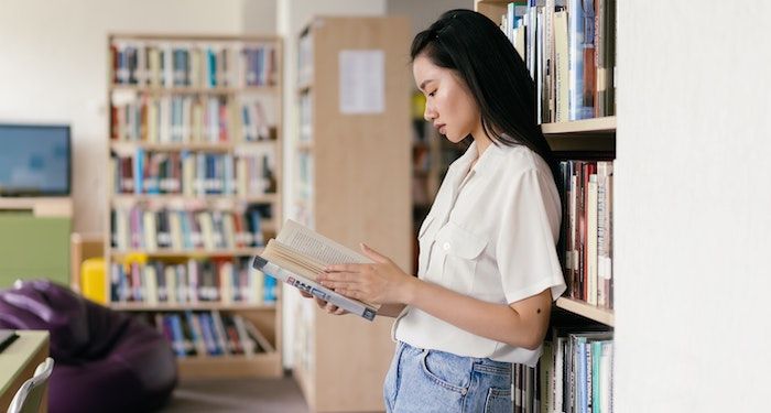 a photo of a young person in a library, holding a book