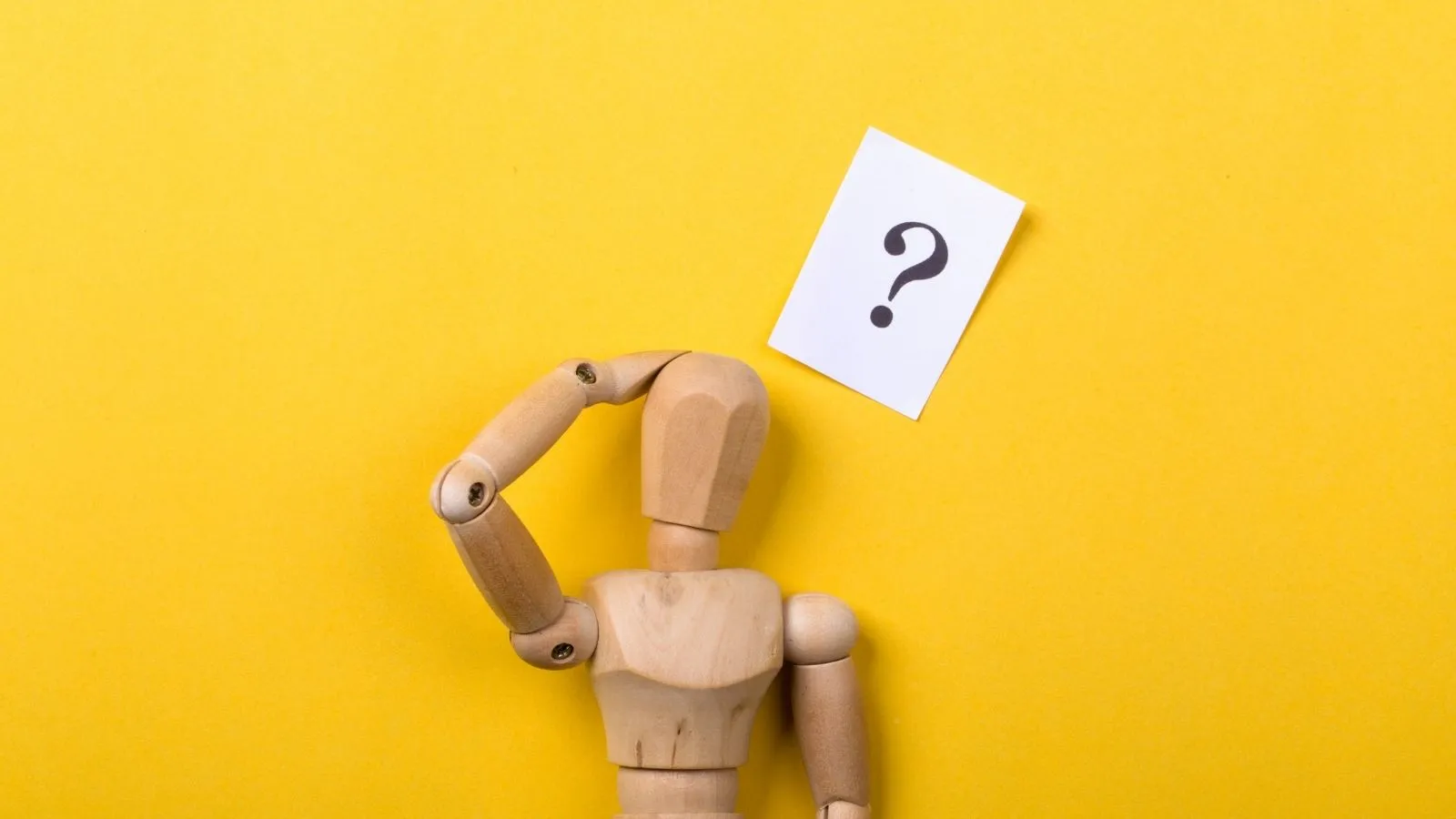 a small wooden mannequin with a question mark above it and one hand held up to its head as is in confusion or wonder.