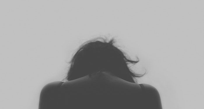 a greyscale photo of a woman's head and shoulders from behind, slouched forward