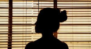 a photo of a woman silhouetted in a window with blinds