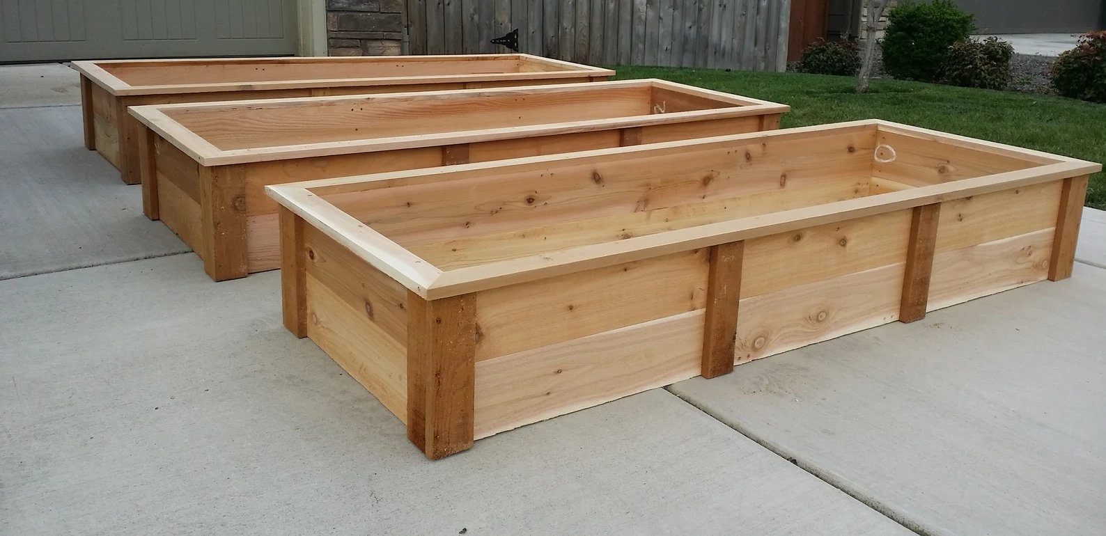 Three large rectangular cedar raised garden beds sit on a driveway.