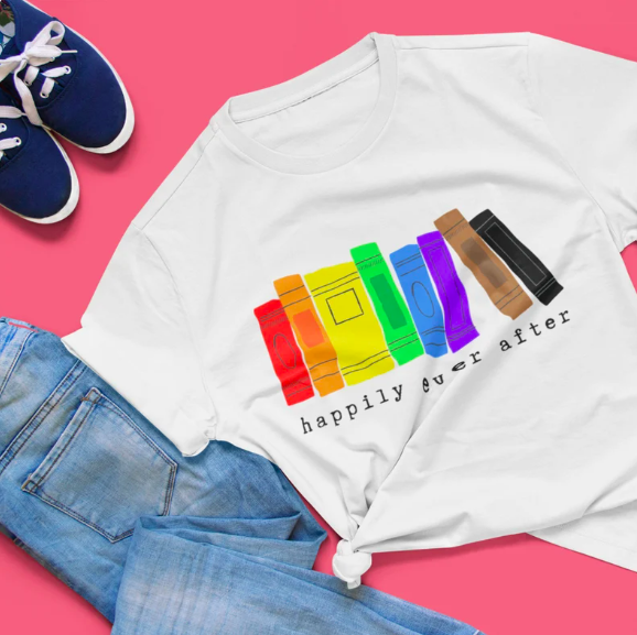 White t-shirt with rainbow books and text "Happily Ever After" screenprinted on it, on a pink background next to jeans and shoes