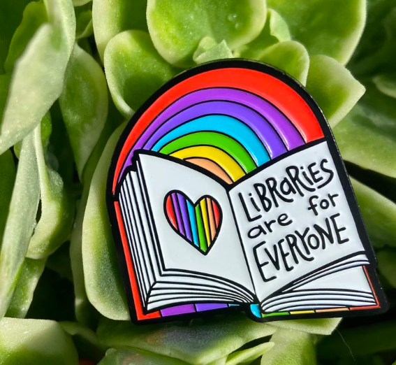 Enamel pin shaped like a book and rainbow that says 