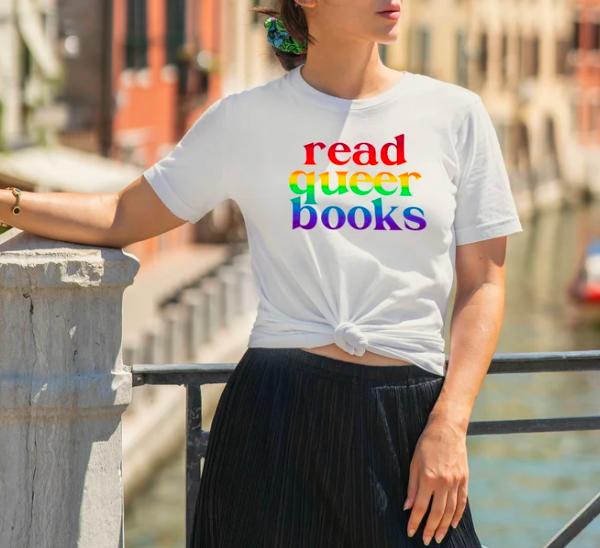 Photo of woman modeling a white t-shirt with "read queer books" in screenprinted in rainbow font