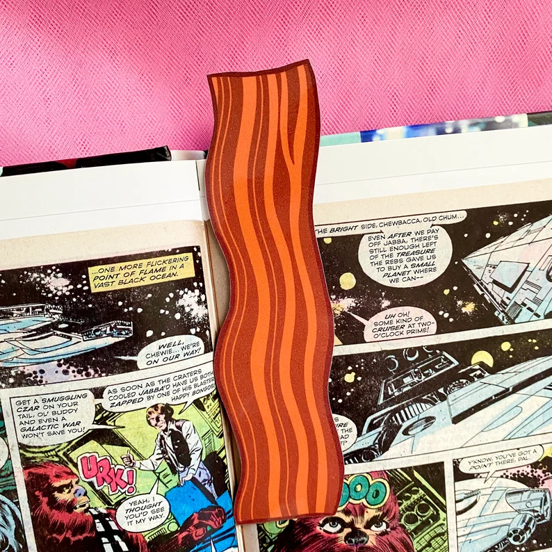 Image of a bookmark in the shape of a strip of bacon in an open comic book. 