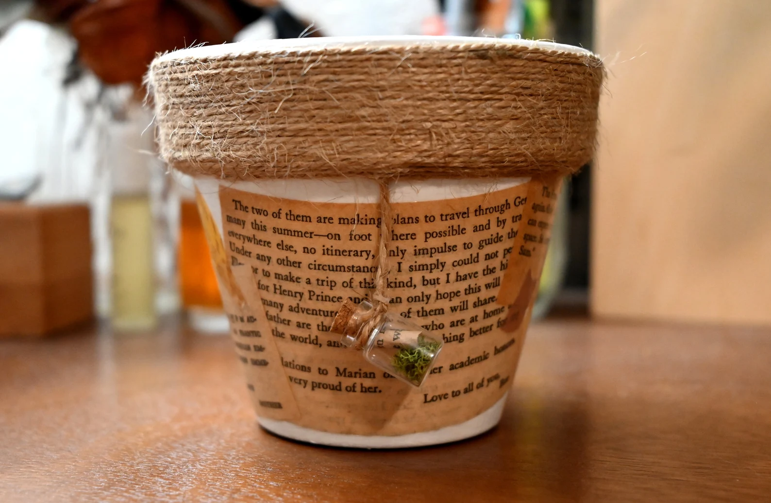 A small pot decorated with pages of text from an old book, and a border of twine wrapped around the top edge.