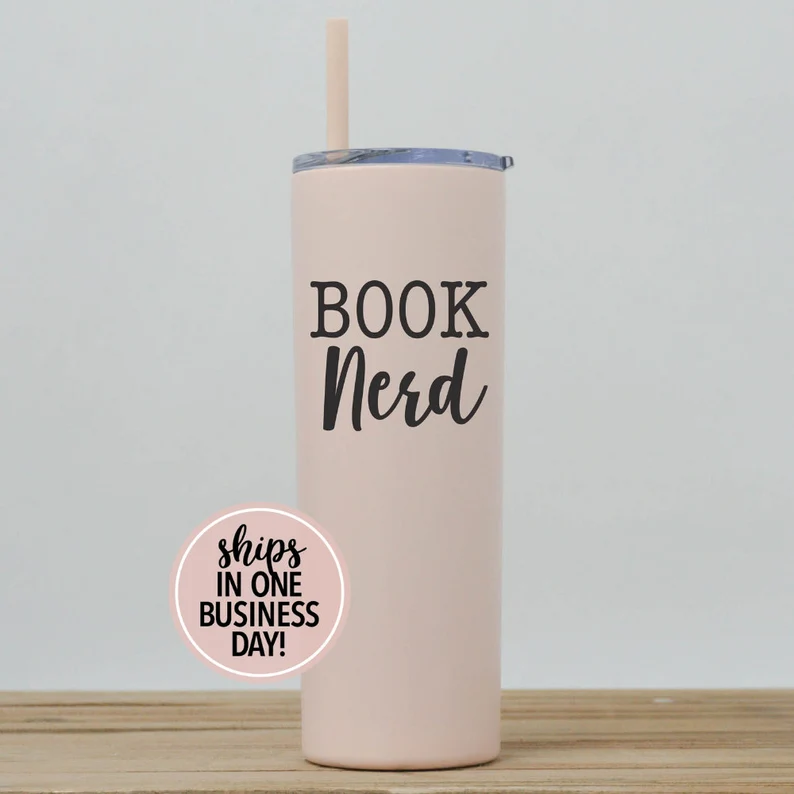 A light pink tumbler with black text that reads "book nerd."