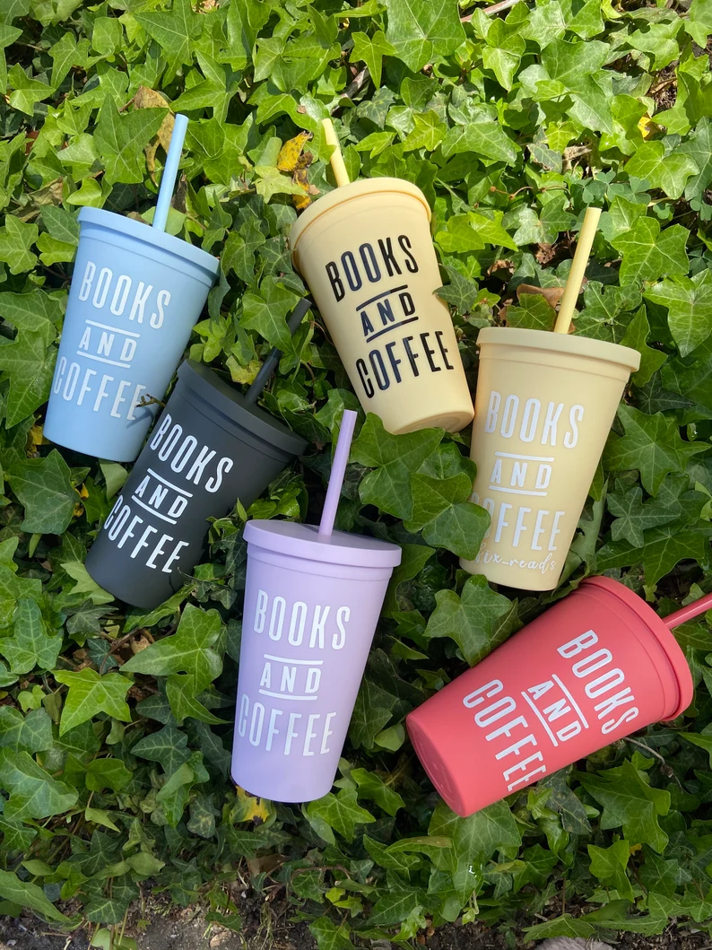 Image of several colorful tumblers on an ivy background. The tumblers all have white font that reads "books and coffee."