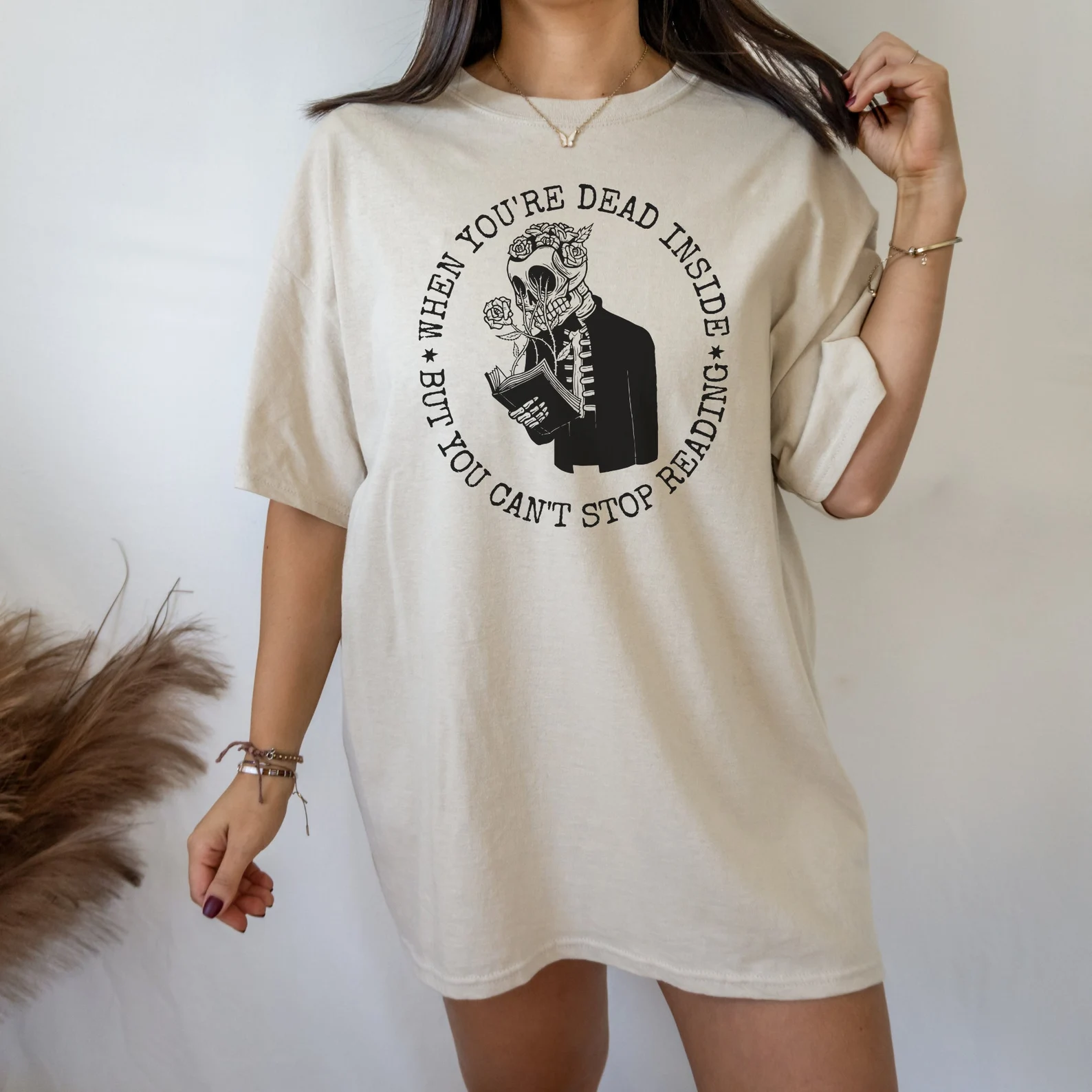 Cream t-shirt with a skeleton reading a book and the words "When you're dead inside but you can't stop reading"