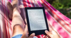 a light-skinned person lying on a pink hammock and holding an ereader