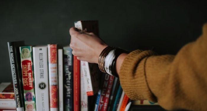 light-skinned hand reaching for books