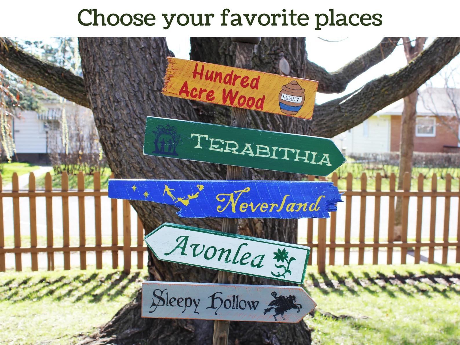 Several colorful hand-painted wooden signs are nailed to a large tree. Places names from books—Hundred Acre Wood, Terabithia, Neverland, Avonlea, Sleepy Hollow—are written on each sign in different fonts.