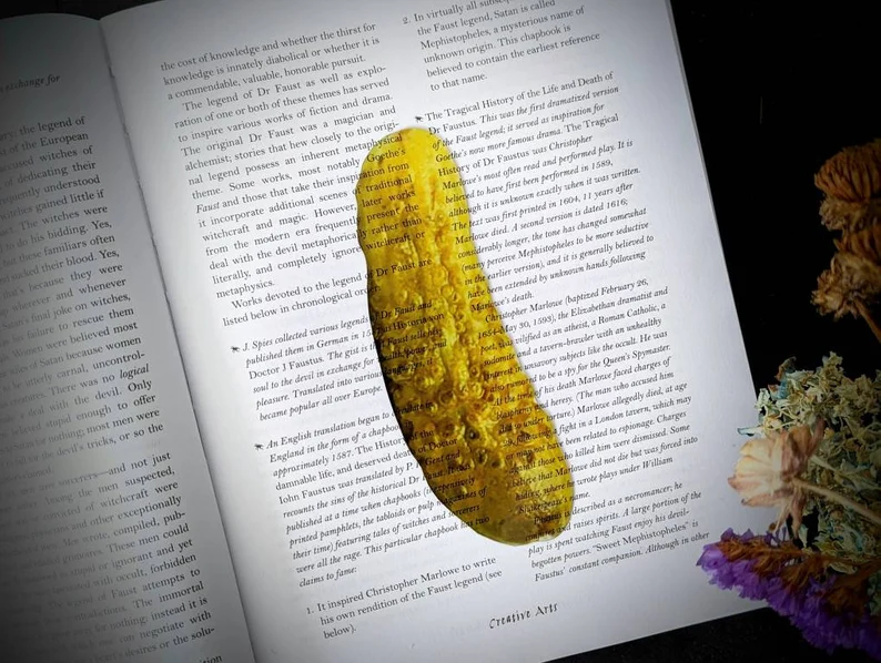 Image of a see-through pickle bookmark on top of a book. 