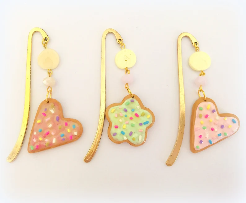 Image of three bookmarks, all with long gold hooks featuring cookie-shaped charms made out of polymer clay. 
