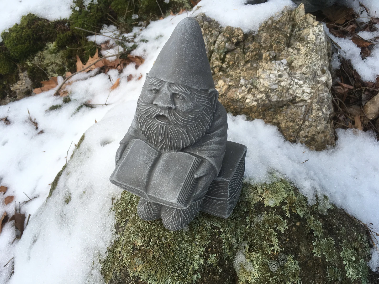 A small silver statue of a gnome with a long beard and pointed hat, sitting on a stack of books with another open book in his hands.