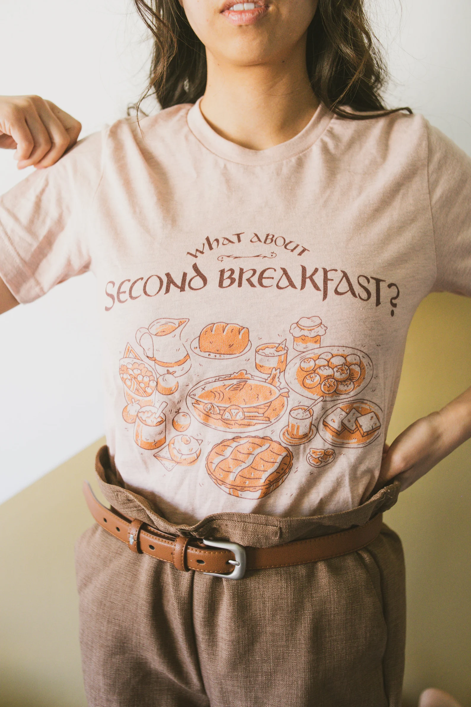 A cream colored t-shirt that reads "What about second breakfast?" and illustrations of cozy breakfast foods