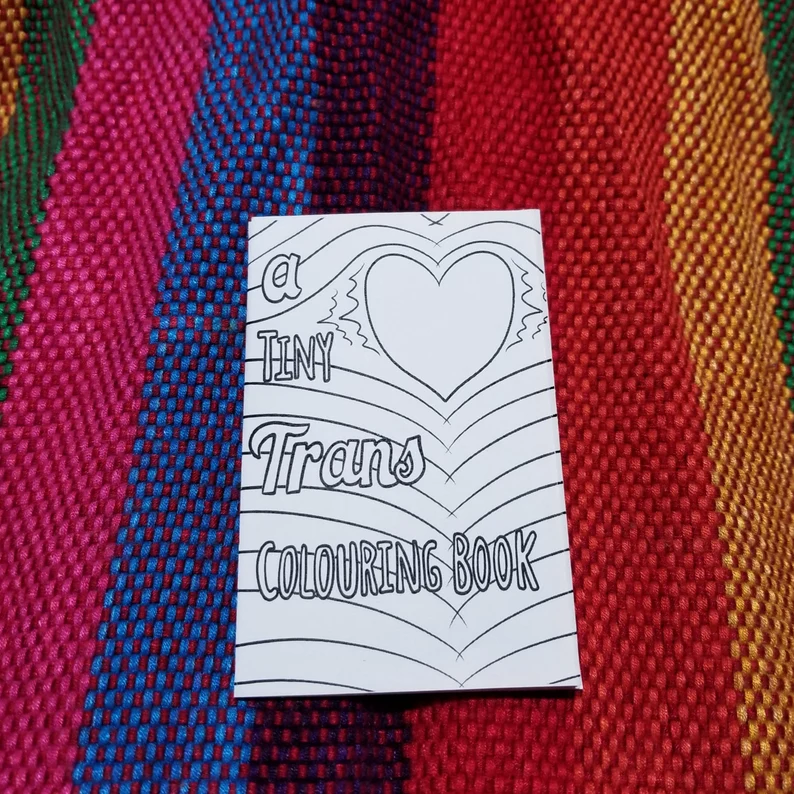 Image of a tiny trans coloring book on a rainbow background