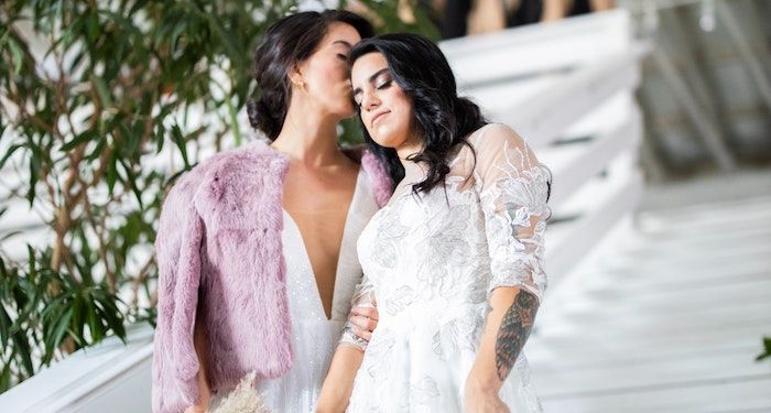 a photo of two women in wedding dresses, one kissing the other on her head