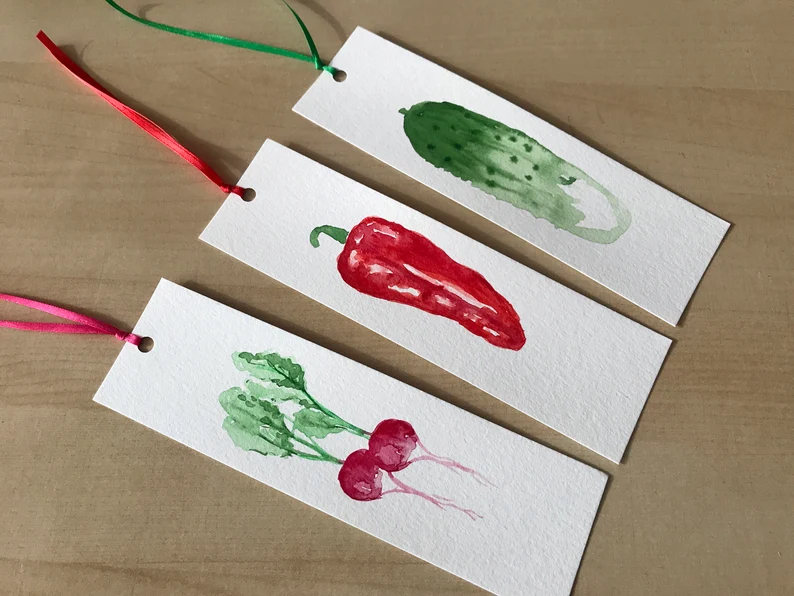 Image of three bookmarks in a row. Left to right are watercolored radishes, a pepper, and a pickle.