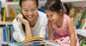 lightly tan-skinned Asian woman smiling and reading with child