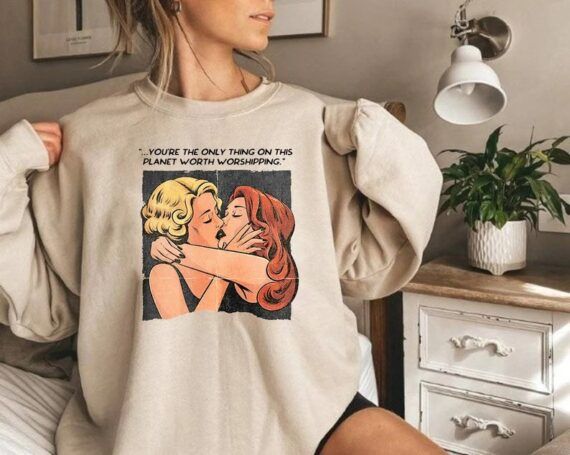 Sweatshirt with a Celia St. James and Evelyn Hugo kissing illustration and the quote, "you're the only thing on this planet worth worshipping"