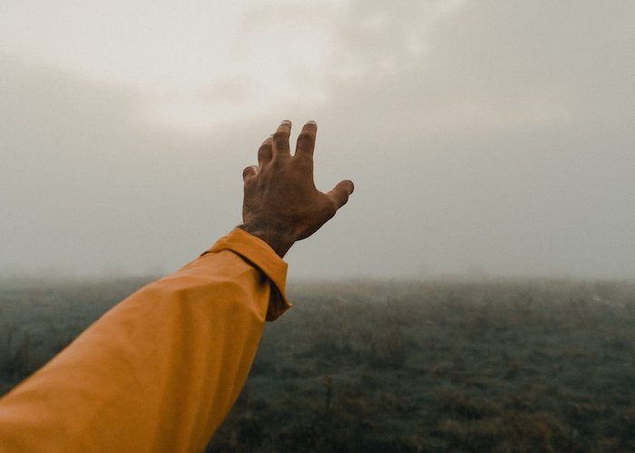 a photo of a hand with brown skin reaching toward a cloudy sky