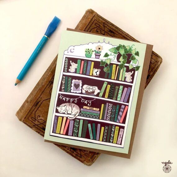 Greeting card with bookcase, cat, and sign that says "Happy Day"