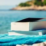 beach reads: a paperback on blue towel with a body of water in the background