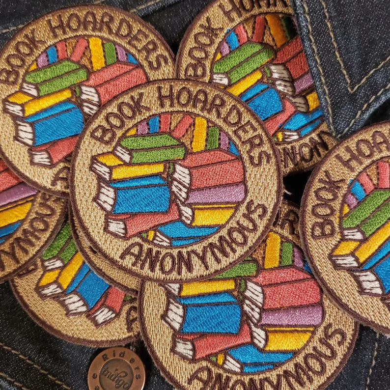 Pile of round patches. The patches feature a pile of books with the words "book hoarders anonymous."