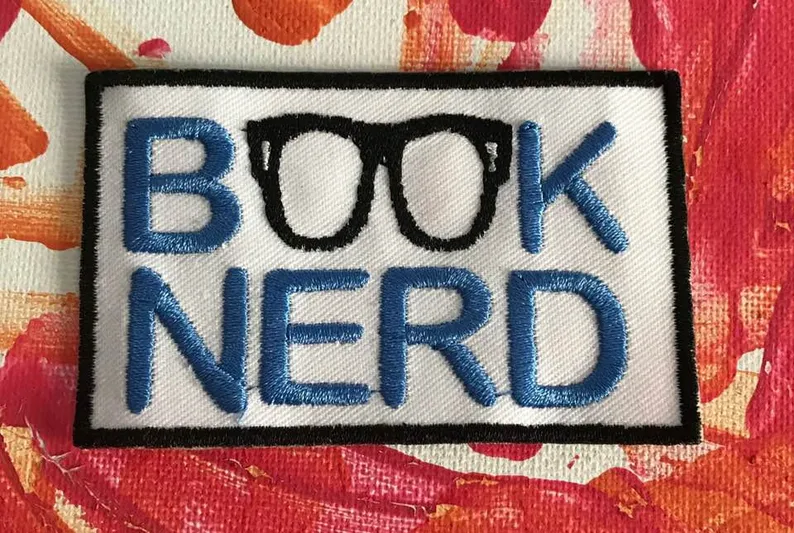 Image of a patch that reads "book nerd." The "oo" in book features a pair of black rimmed glasses. 