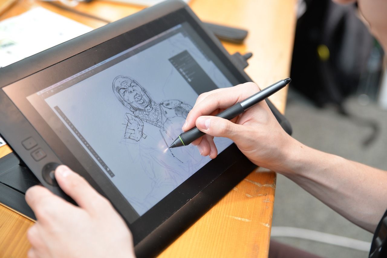 Close up of two hands and a graphics tablet. An artist is drawing a shouting figure on the tablet's screen.