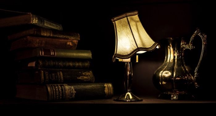 a tiffany lamp next to a pile of old books in dark lighting