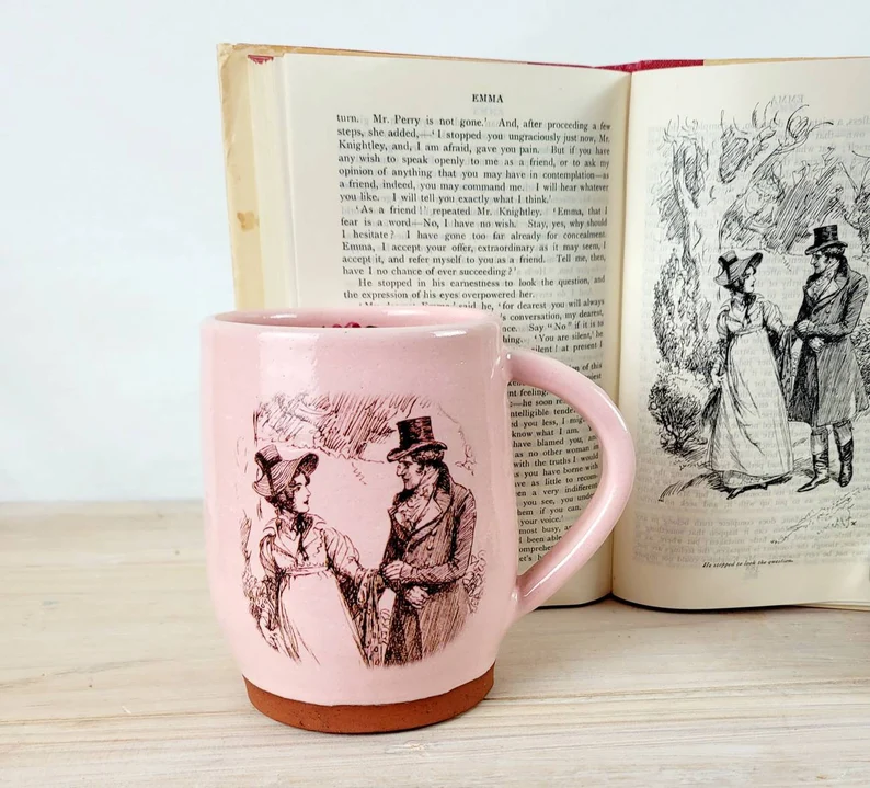 photo of a pink mug with a drawing from Emma in front of an open page with the book with the same illustration