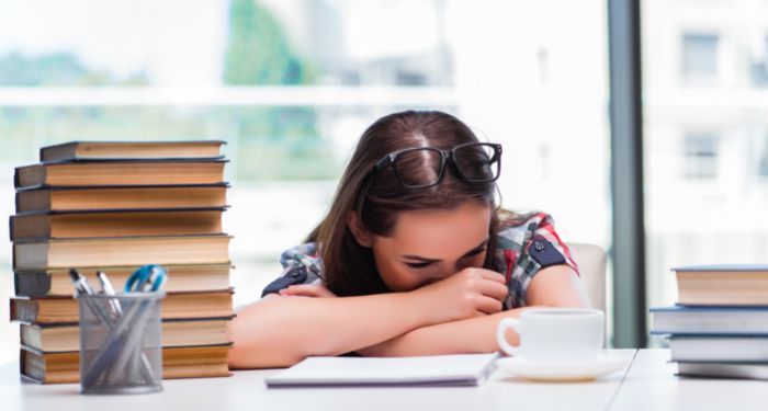 Image of a woman hiding her face besidee a stack of books