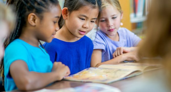 three kids of differing skin tones sitting next to each other and reading the same book