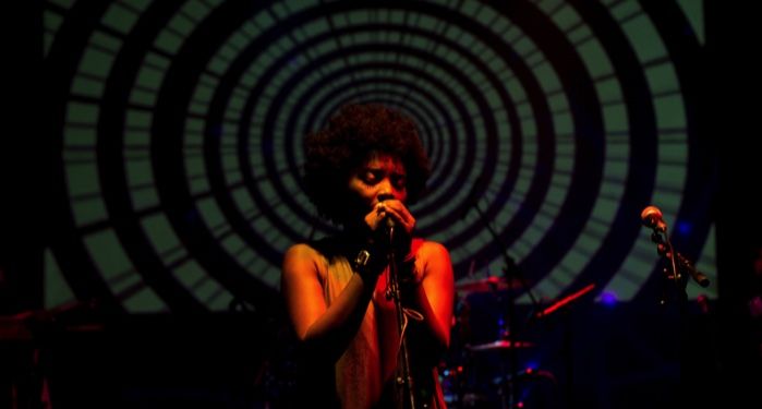 a woman with Brown skin and an afro singing into a microphone