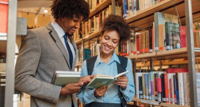 a brown-skinned Black man and woman reading from a book and smiling