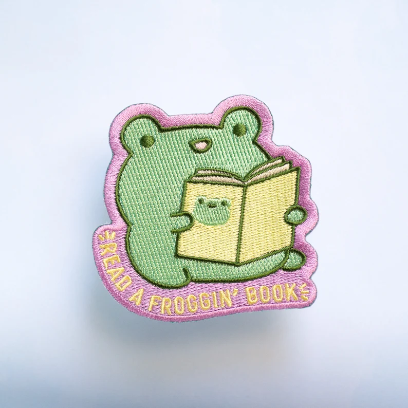 image of a frog-shaped patch. The frog is reading a book.