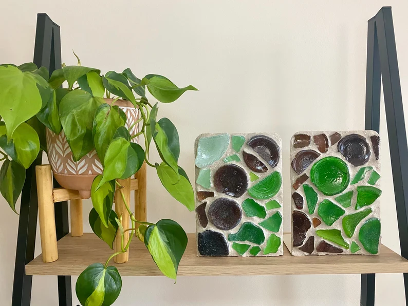 Image of 2 green sea glass bookends on a shelf with a plant. 