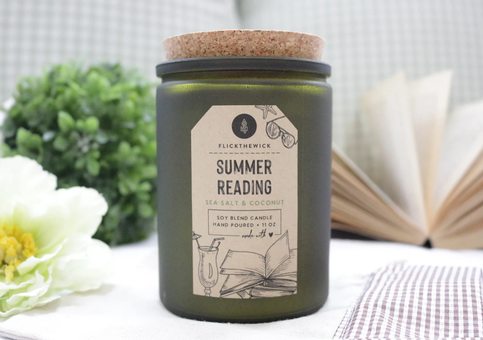 A tall green glass jar candle with a brown label that reads "Summer Reading — Sea salt and coconut soy candle"